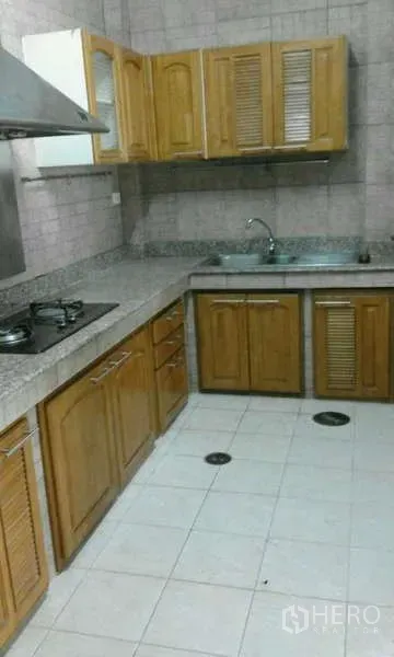 Townhouse for rent in Suan Luang, Bangkok - L-shaped kitchen with wooden cabinets, granite countertops, gas hob, range hood and stainless sink.