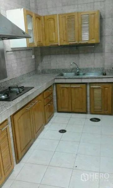 Townhouse for rent in Suan Luang, Bangkok - L-shaped kitchen with wooden cabinets, granite countertops, gas hob, range hood and stainless sink.