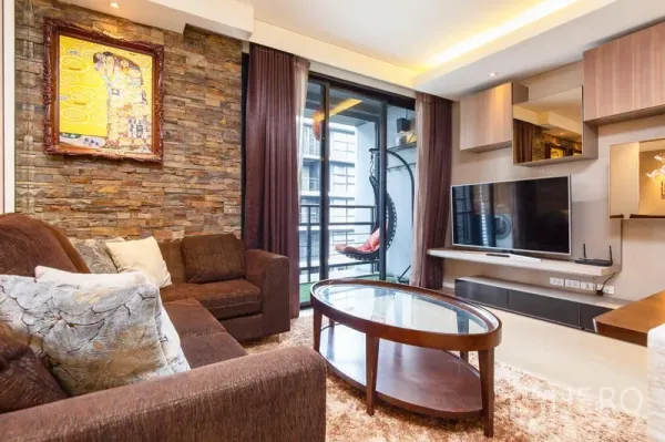 Condominium for rent in Watthana, Bangkok - Media wall with mounted TV and built-in cabinets beside sliding doors to a balcony with a hanging chair.