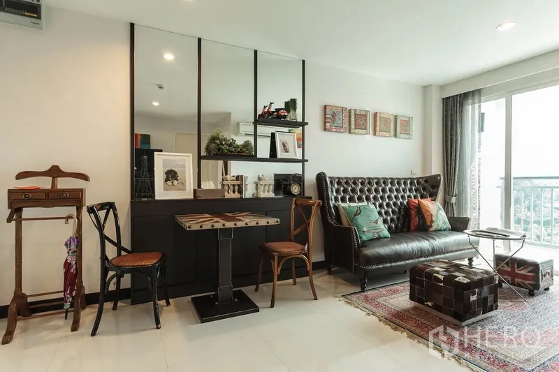 Condominium for rent in Khlong Toei, Bangkok - Cozy lounge with tufted leather sofa, mirrored wall, and sliding doors to the balcony.