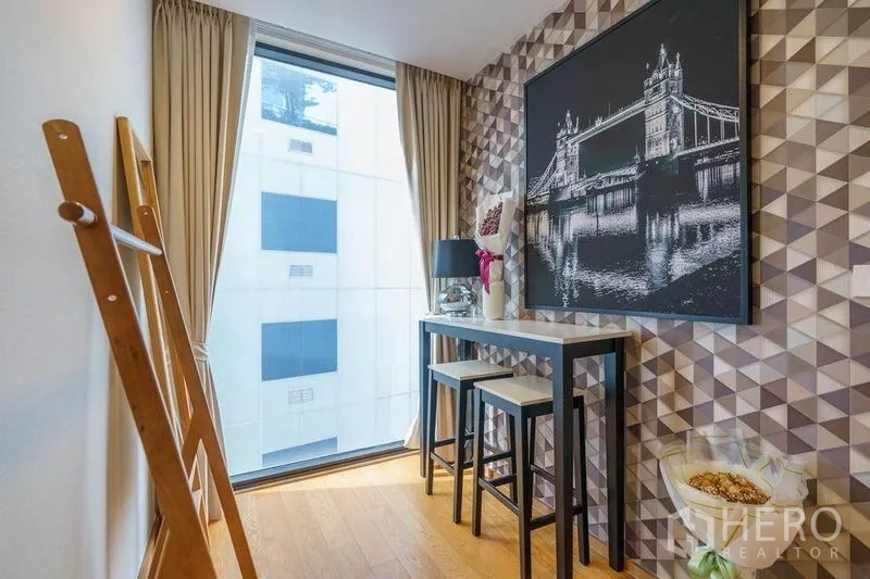 公寓 出租或出售在Bang Rak, Bangkok - 小型吧台与高脚凳，几何壁纸背景，旁为高窗采光。