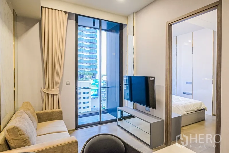 Condominium for rent in Watthana, Bangkok - Living area with TV console, sliding glass door to the balcony and doorway leading to the bedroom.