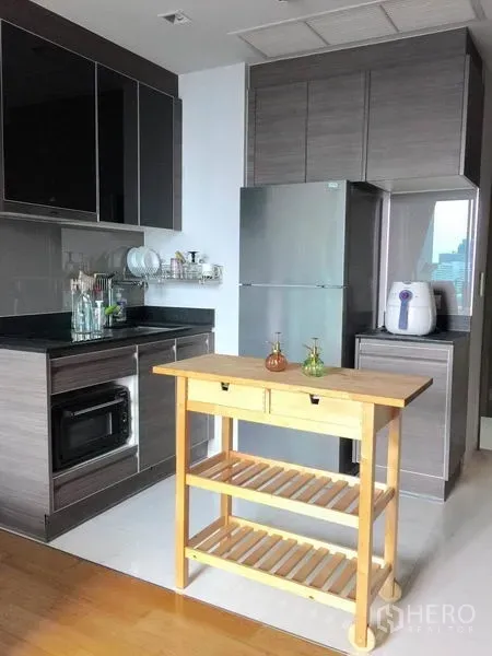 Condominium for rent in Khlong Toei, Bangkok - Modern kitchen with grey cabinets, countertop appliances, fridge and a wooden island cart.
