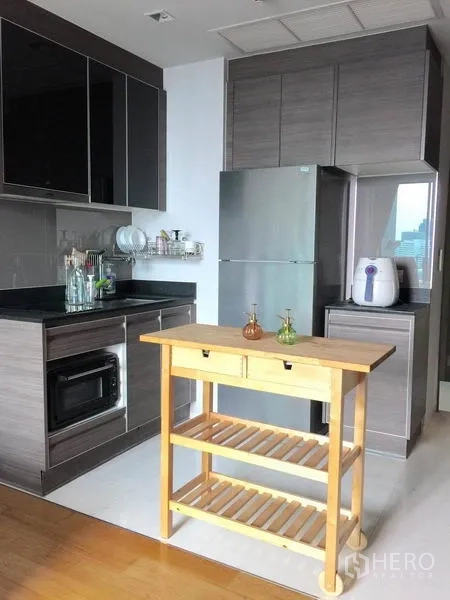 Condominium for rent in Khlong Toei, Bangkok - Modern kitchen with grey cabinets, countertop appliances, fridge and a wooden island cart.