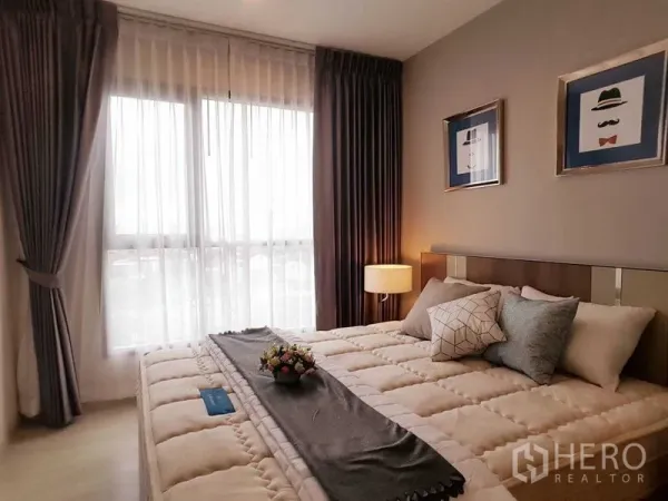 Condominium for sale in Khlong Toei, Bangkok - Cozy bedroom with cushioned bed, bedside lamp, and sheer curtains over a large window.
