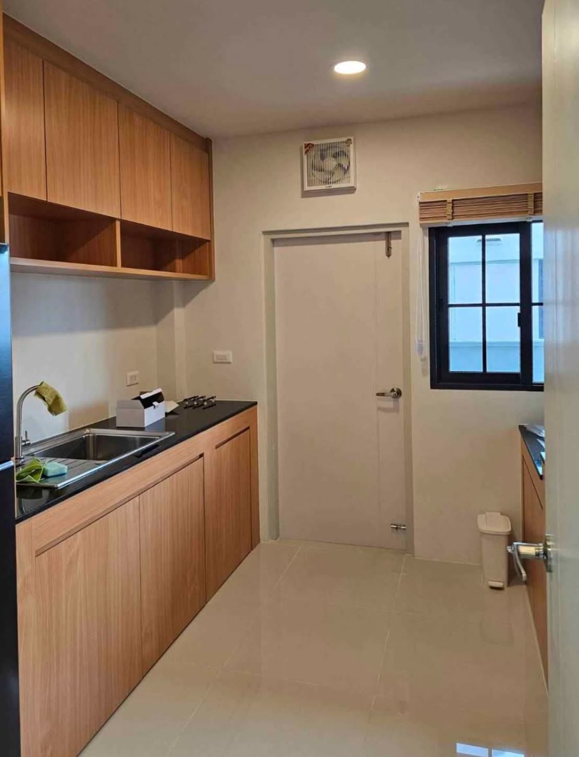 Detached House for rent in Bang Phli, Samut Prakan - Closed kitchen with wood cabinetry, black stone countertops, sink, gas hob and a window for ventilation.