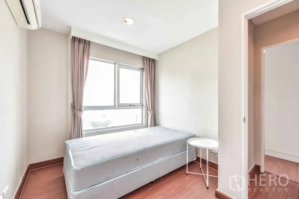 คอนโด for rent in Huai Khwang, Bangkok - ห้องนอนสว่างพร้อมเตียงเดี่ยว หน้าต่าง ผ้าม่าน และโต๊ะข้างเตียง