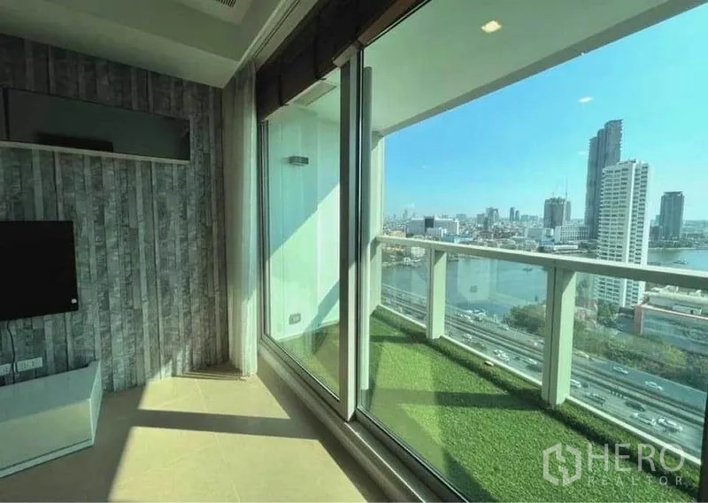 Condominium for rent in Khlong San, Bangkok - Living area with floor‑to‑ceiling sliding doors opening to a balcony with Chao Phraya River and skyline views.