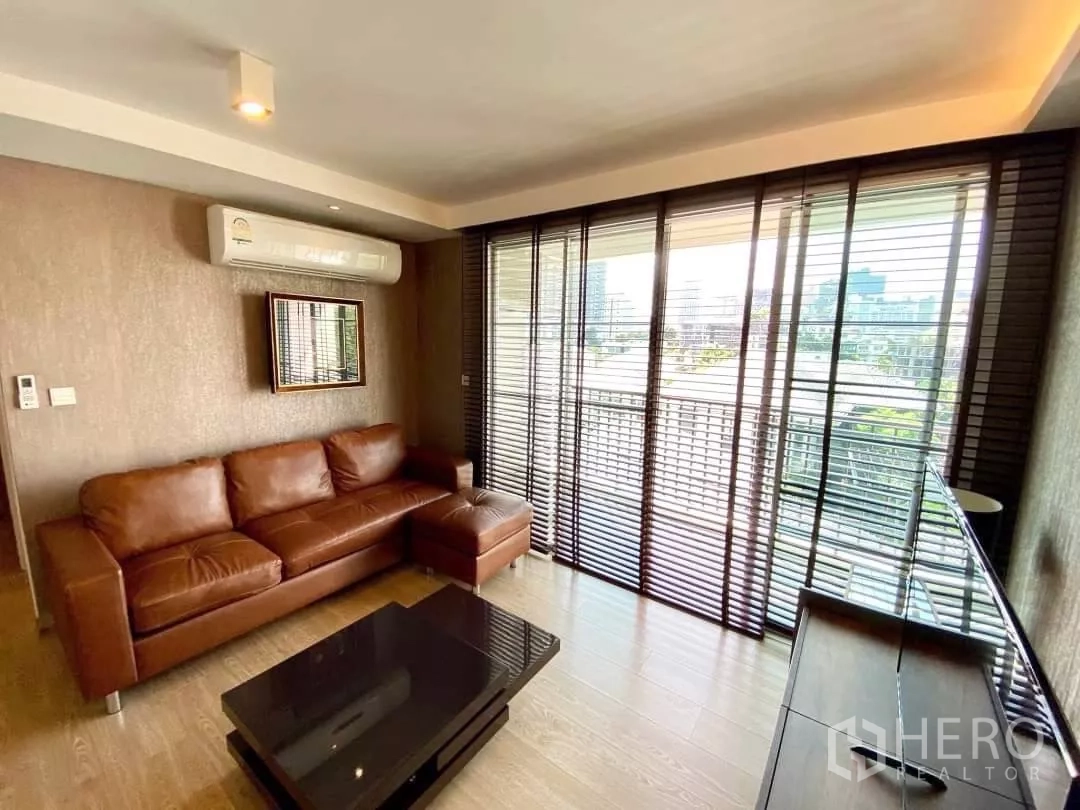 公寓 出租在Watthana, Bangkok - 客厅棕色皮沙发，面对电视并通往阳台