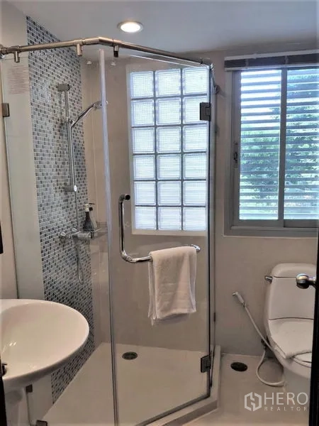 Condominium for rent in Bang Rak, Bangkok - Modern bathroom with a glass shower enclosure and window.