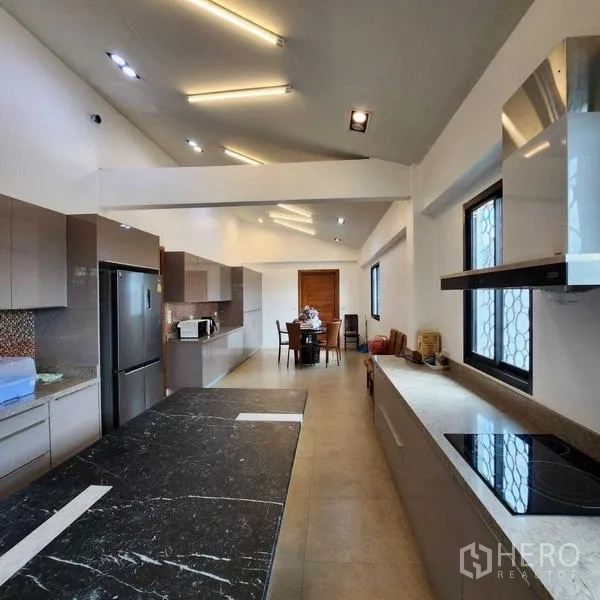 独立式住宅 出售在Phra Khanong, Bangkok - 长形开放式厨房，黑色岛台、嵌入式柜体与尽头餐区