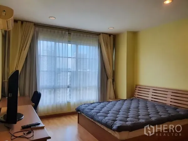 Condominium for rent in Khlong Toei, Bangkok - Primary bedroom with large window, desk, wood floors and queen bed.