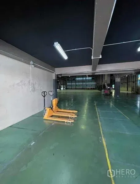 Warehouse for rent in Si Racha, Chon Buri - Ground-level storage zone with pallet jacks and strip lighting inside the warehouse.
