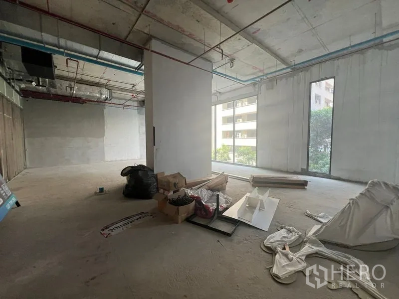 零售空间 出租在Khlong Toei, Bangkok - 开放式毛坯商铺，水泥地面，大面积采光窗，可见周边建筑景观。