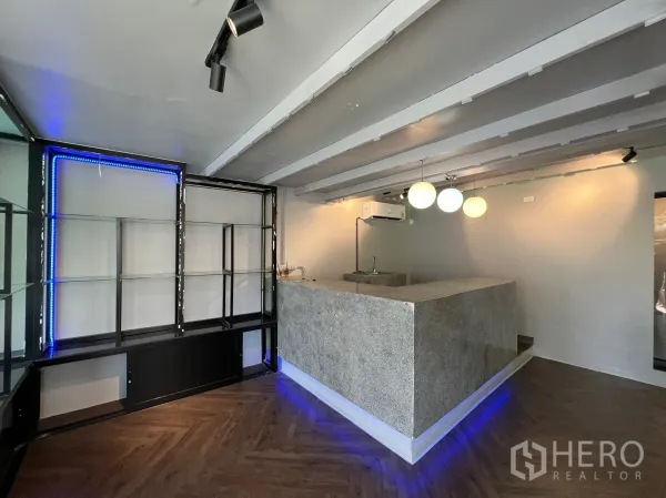 Retail Space for rent in Watthana, Bangkok - Retail area with a stone service counter, pendant lights and metal-and-glass display shelves highlighted by blue LED strips.
