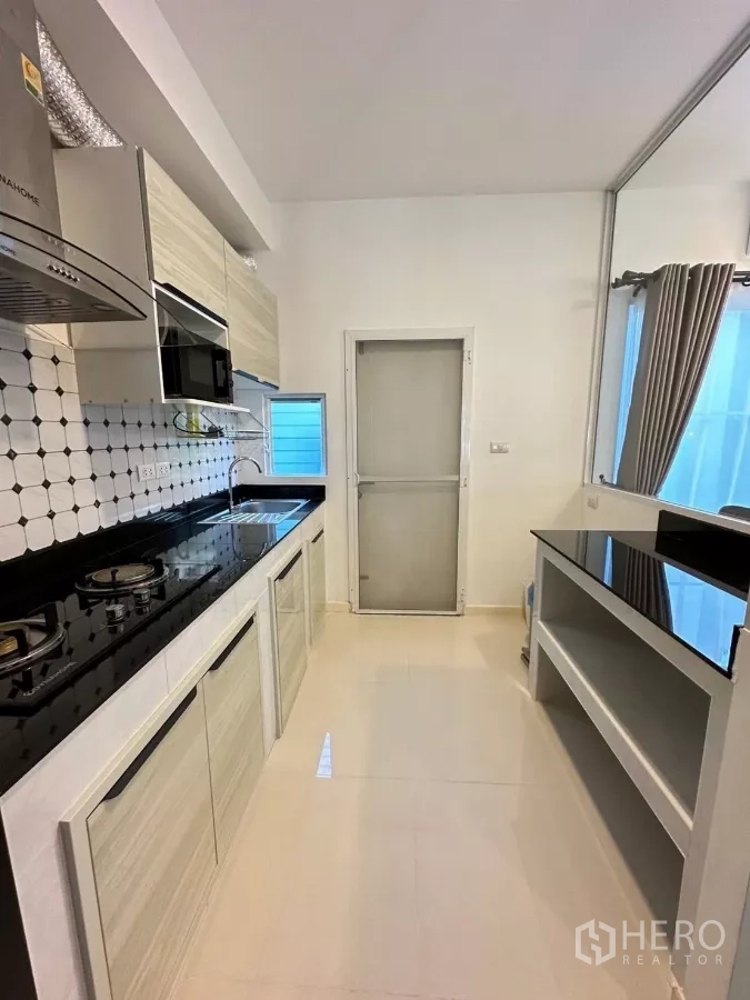 Townhouse for rent in Bang Phli, Samut Prakan - Modern galley kitchen with gas hob, hood, microwave and black countertops.