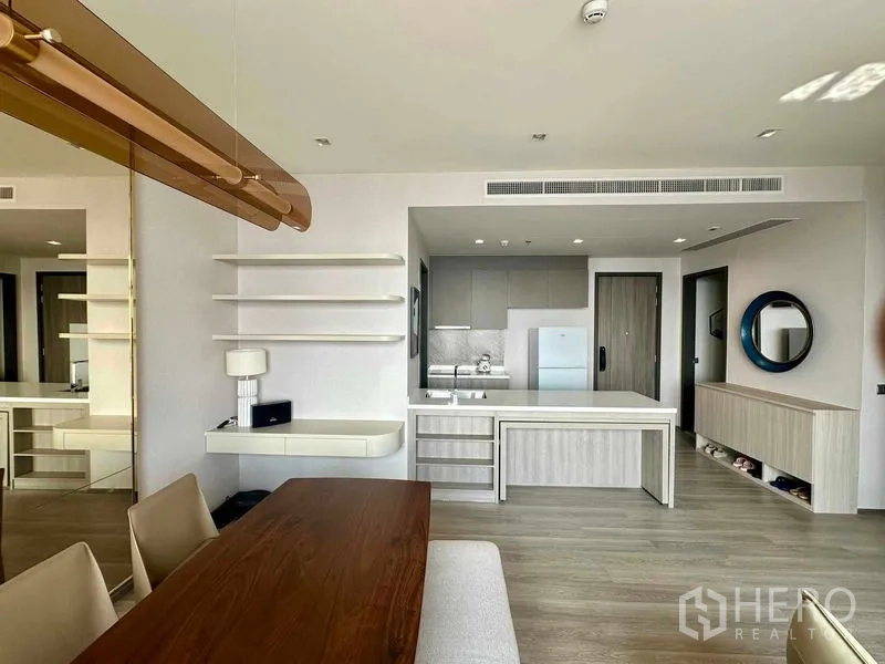 Condominium for rent in Bang Kho Laem, Bangkok - View from dining to kitchen showing floating shelves, large island and neutral wood finishes.