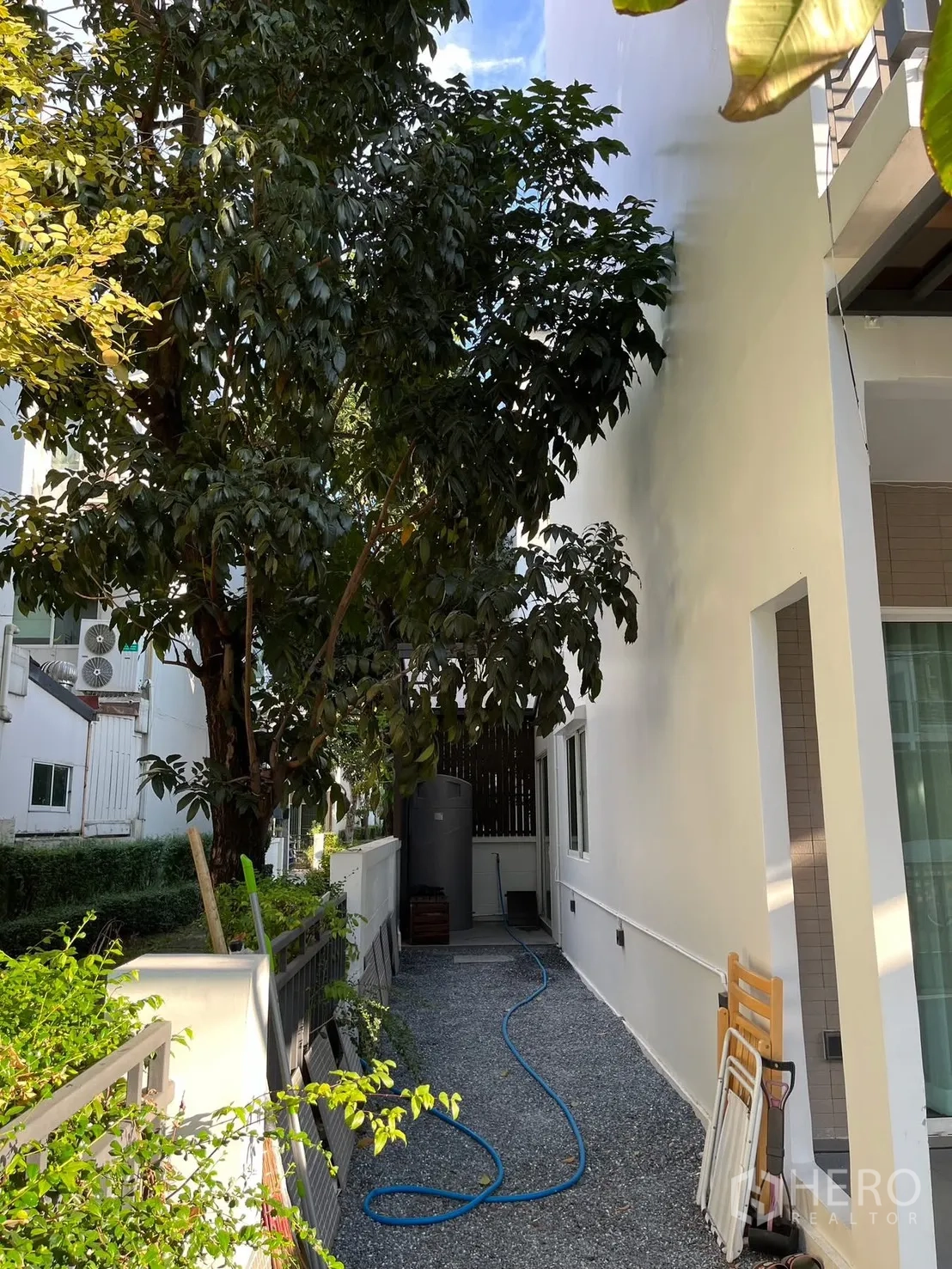联排别墅 出租在Prawet, Bangkok - 侧院碎石小径，茂盛树木与储水罐区域
