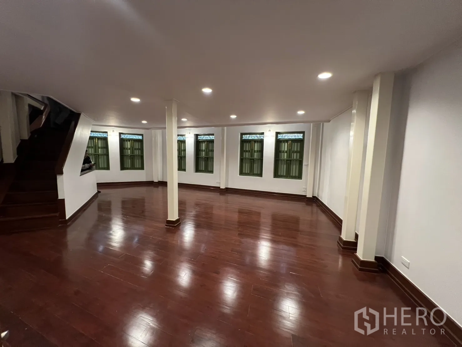 店屋 for rent in Samphanthawong, Bangkok - 二层宽敞空间，抛光木地板、筒灯、承重柱与绿色百叶窗，旁有楼梯，适合办公或展示。