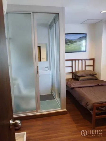 Shophouse for rent in Watthana, Bangkok - Bedroom with frosted glass sliding door to the bathroom and wood flooring.
