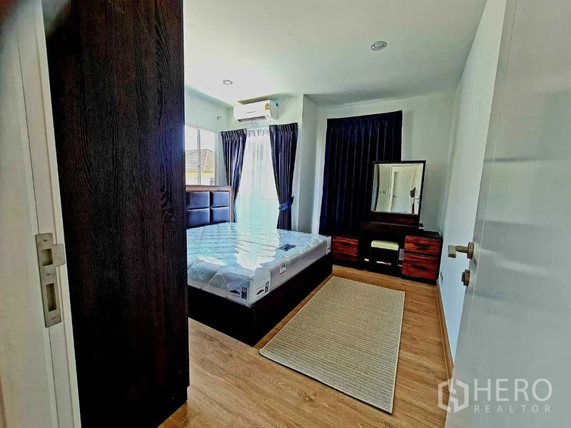 Detached House for rent or sale in Pathum Thani - Bright bedroom with large windows, air conditioner, dressing table and warm wood flooring.