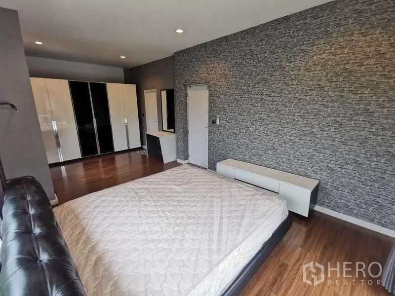 บ้าน ให้เช่าในPrawet, Bangkok - มุมห้องนอนใหญ่พร้อมผนังลายหิน ชั้นวางทีวี โต๊ะเครื่องแป้ง และตู้เสื้อผ้ามันวาว