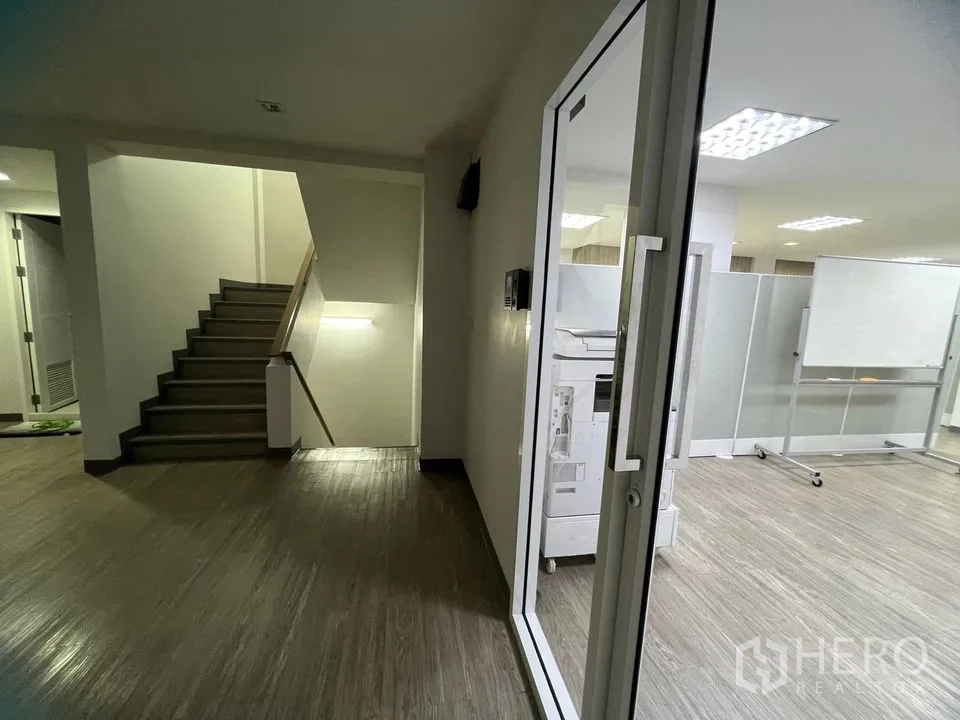 零售空间 出租在Watthana, Bangkok - 走廊带楼梯与玻璃门，木纹地板通往办公区。