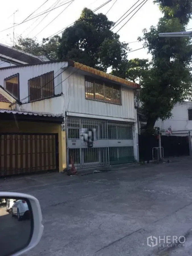 Townhouse for sale in Watthana, Bangkok - Two-storey townhouse exterior in Watthana with metal sliding gate, barred windows and a quiet lane with trees near BTS Ekkamai.