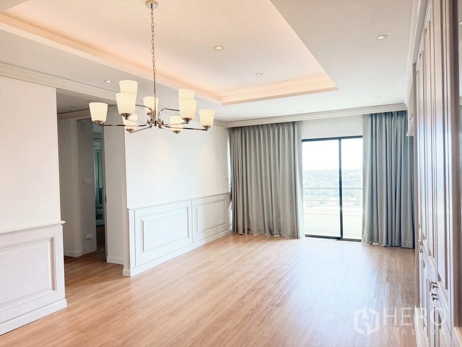 Condominium for rent or sale in Sathon, Bangkok - Bright living room with tray ceiling, chandelier and sliding glass door to balcony.