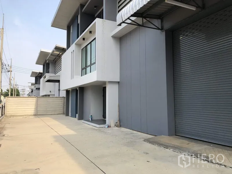 Warehouse for rent or sale in Lam Luk Ka, Pathum Thani - Wide driveway beside the unit with large roller shutter loading bay and canopy, suitable for truck access.