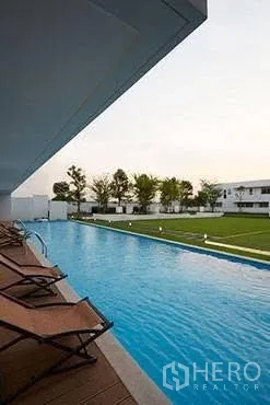 Detached House for rent in Saphan Sung, Bangkok - Long communal swimming pool with sun loungers beside a green lawn.