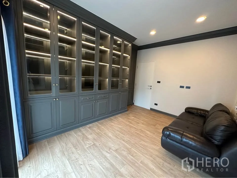 Detached House for rent in Bang Kapi, Bangkok - Room with floor-to-ceiling illuminated built-in shelving and a leather sofa.