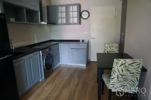 Condominium for sale in Khlong Toei, Bangkok - Open kitchen with grey cabinets, black countertops, washer-dryer and a two-seat dining table.