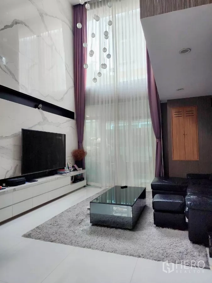 Detached House for rent or sale in Chatuchak, Bangkok - Double-height living room with marble feature wall, large TV, chandelier and sectional sofa.