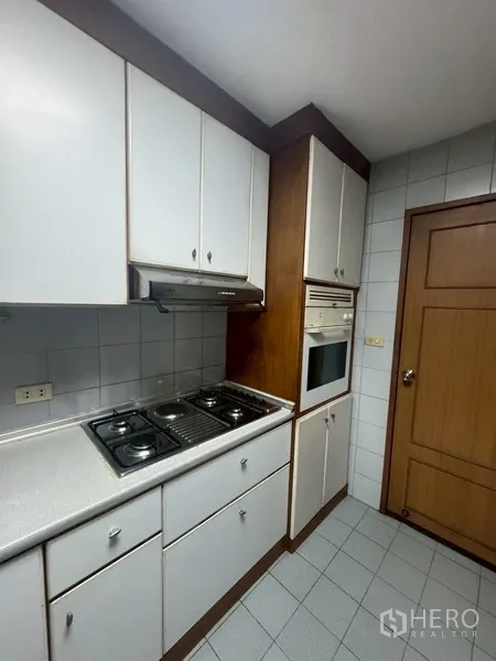 Condominium for rent in Watthana, Bangkok - Close-up of kitchen cooktop, range hood, and built-in oven against tiled walls.