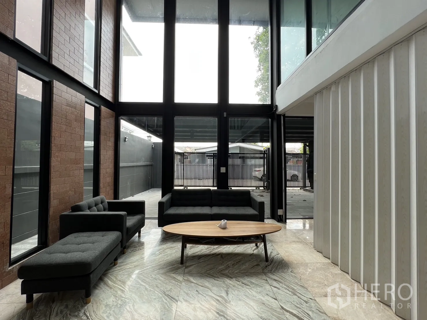 Detached House for rent or sale in Phra Khanong, Bangkok - Living area facing the front yard through tall black-framed glazing and sliding doors.