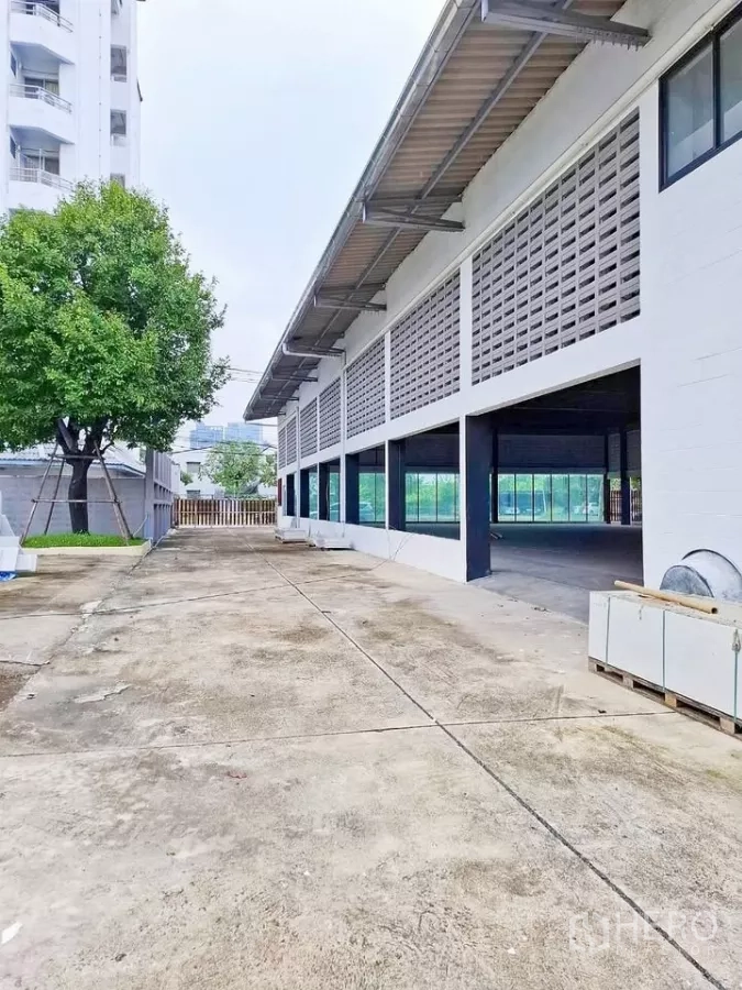 Warehouse for rent in Bang Kapi, Bangkok - Long driveway along the warehouse with canopy eaves, windows and gated truck access.