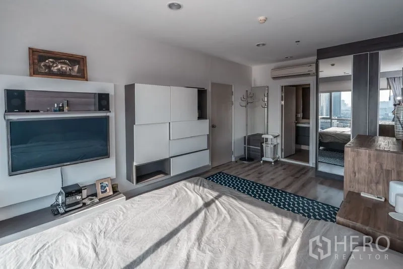 Condominium for rent in Sathon, Bangkok - Spacious bedroom angle showing wall-mounted TV, mirrored wardrobe, and air-conditioning.