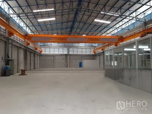 货栈 出租在Mueang Samut Prakan, Samut Prakan - 仓库地面设有橙色桥式起重机跑道梁，侧边为玻璃隔断办公室，采光充足。