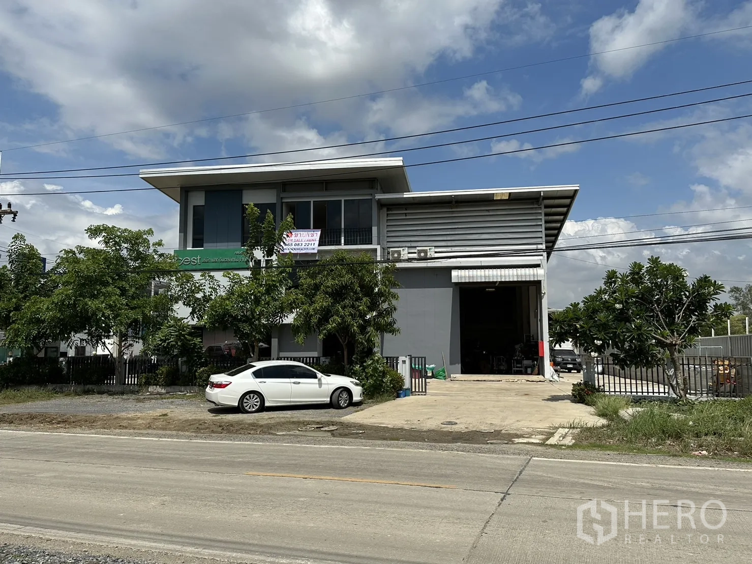 Factory for rent or sale in Pathum Thani - Front elevation of the mini factory with signboard and mature trees.