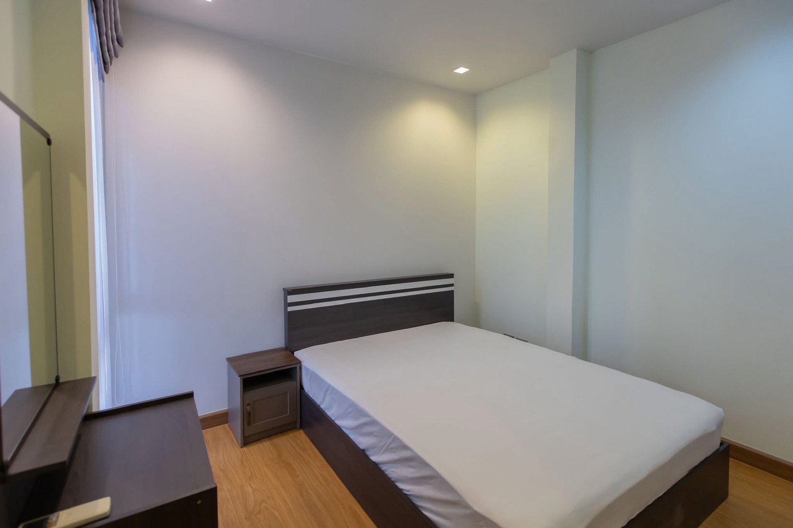 Detached House for rent in Lat Phrao, Bangkok - Simple guest bedroom with double bed, wood flooring, bedside table, and vanity.