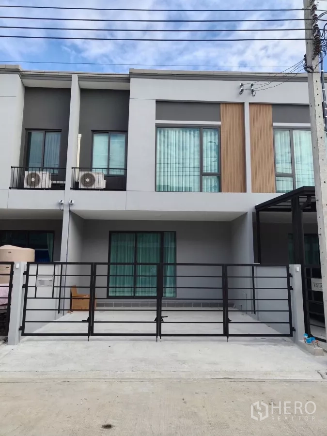 Townhouse for rent in Bang Phli, Samut Prakan - Modern two-storey townhouse with black metal gate and gated parking under blue sky.