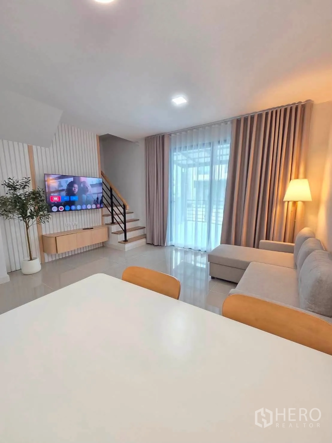 Townhouse for rent in Bang Phli, Samut Prakan - Open-plan living room with sofa, wall-mounted TV, dining table and stairs.