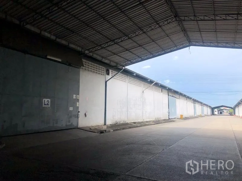 Warehouse for rent in Bang Pa-in, Phra Nakhon Si Ayutthaya - Loading area under a large metal canopy with multiple warehouse entrances along the lane.