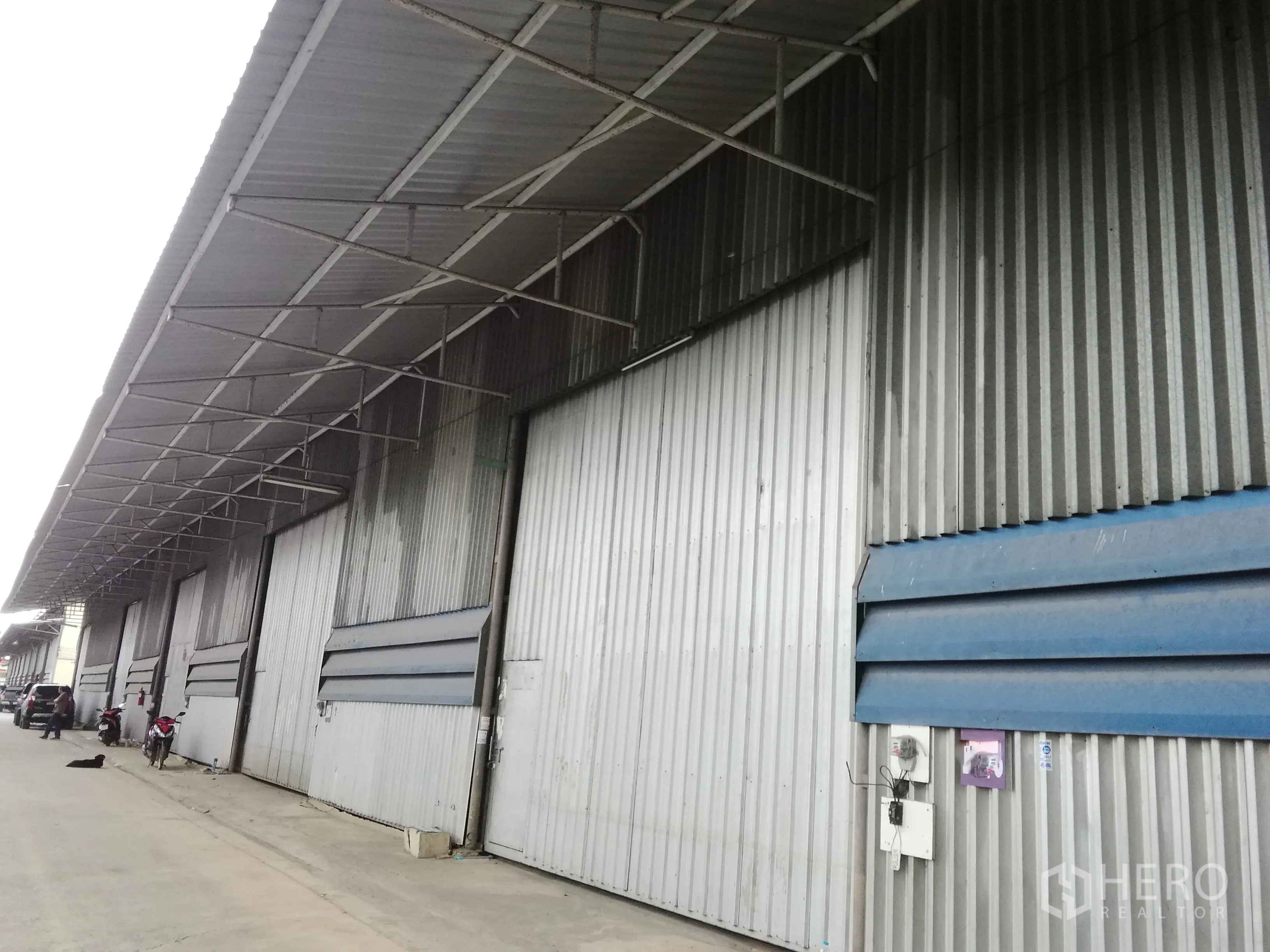 Warehouse for rent in Lam Luk Ka, Pathum Thani - Corrugated metal warehouse facade with a long covered loading bay and multiple large sliding doors in an industrial row.