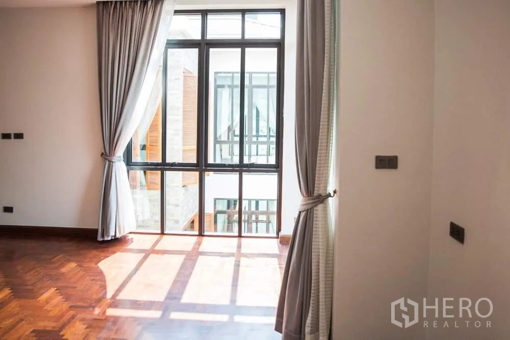 Detached House for rent in Khlong Toei, Bangkok - Sunlit bedroom with gray curtains and a large window facing the inner courtyard.