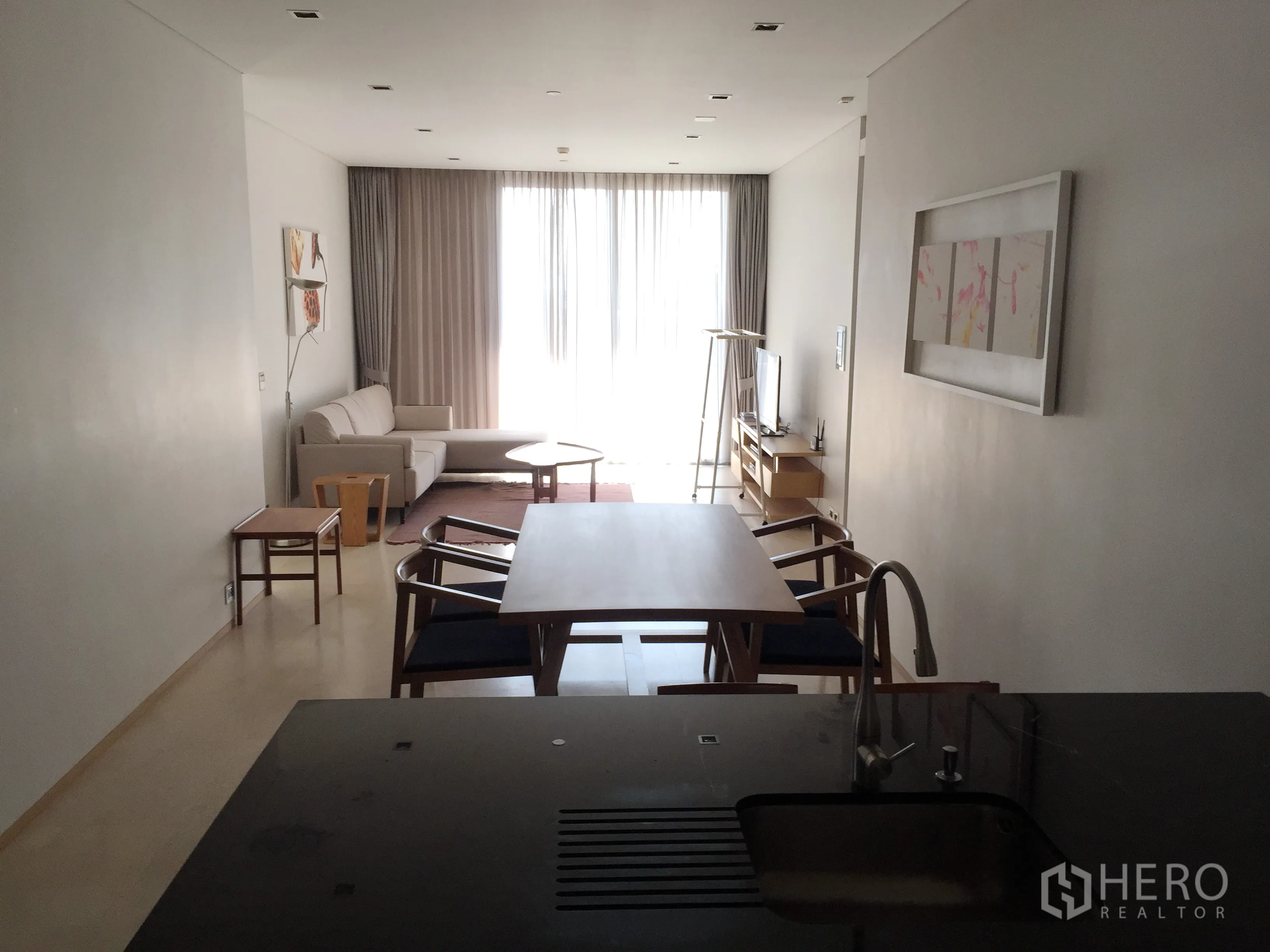 Condominium for rent in Bang Rak, Bangkok - Open-plan living and dining area with kitchen island, sofa, TV console and floor-to-ceiling sheer curtains.
