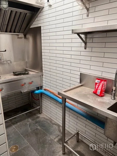 Shophouse for rent or sale in Watthana, Bangkok - Compact stainless prep kitchen with hood, sink and white subway-tile walls.