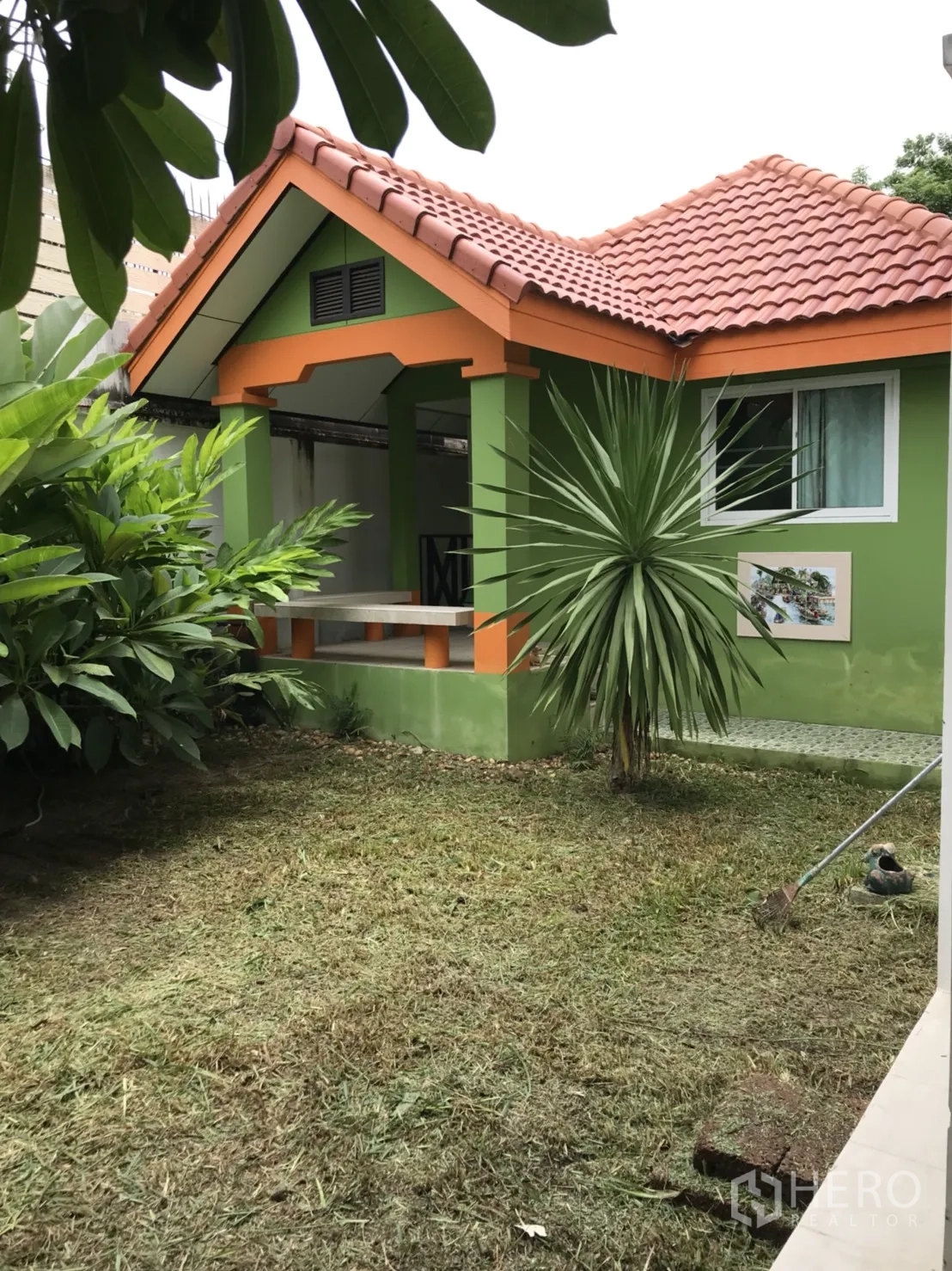 Detached House for rent in Lat Krabang, Bangkok - Detached house exterior with green-and-orange facade, terracotta roof and small lawn with tropical plants.