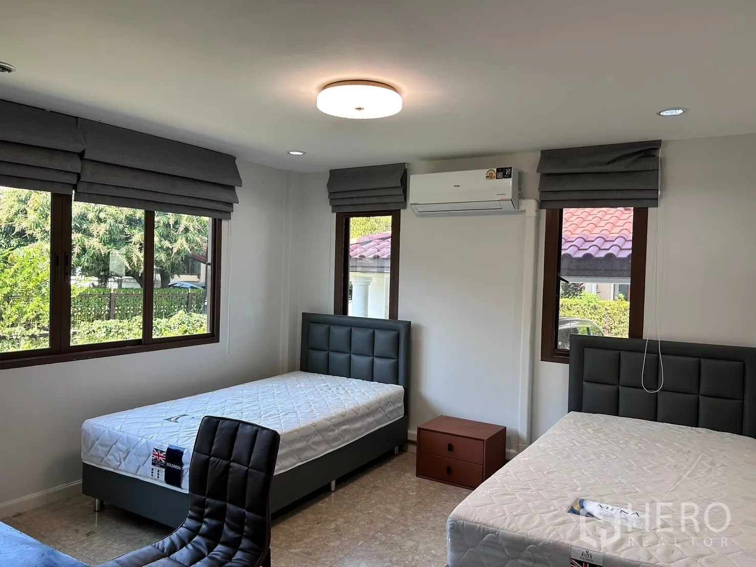 Detached House for rent in Lat Krabang, Bangkok - Bright twin bedroom with large windows, grey Roman blinds, air conditioner and study chair.